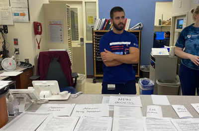 Mike Tomasetti, a nurse manager at Penn Presbyterian Medical Center, stands at a nurse’s station covered with stacks of paper forms.